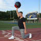 Fitness trainer Kevin Saenz holds a medicine ball above his head as he performs walking lunges down the Hackensack High School track.