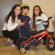 The teens present a bike to a young boy. 