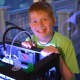 Michael Walding, a seventh-grader at Seven Bridges Middle School, poses for photos beside a 3D printer.